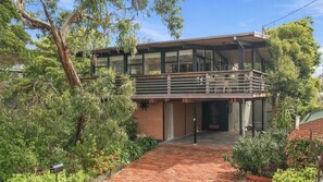 Une maison moderne à deux étages, dotée d’un balcon et entourée d’une végétation luxuriante.