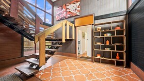 A wooden staircase leading to a second floor, a wall-mounted shelf with various items, and a patterned rug on the floor. - Kathryn Central Retro Coastal Charm, Walk to Beach & Cafés (Inverloch)