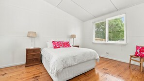 A bedroom with a bed, two bedside tables, a window with blinds, and a wooden floor. - Kathryn Central Retro Coastal Charm, Walk to Beach & Cafés (Inverloch)