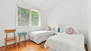 Une chambre avec deux lits simples, une chaise en bois, une petite table et une fenêtre avec des stores.