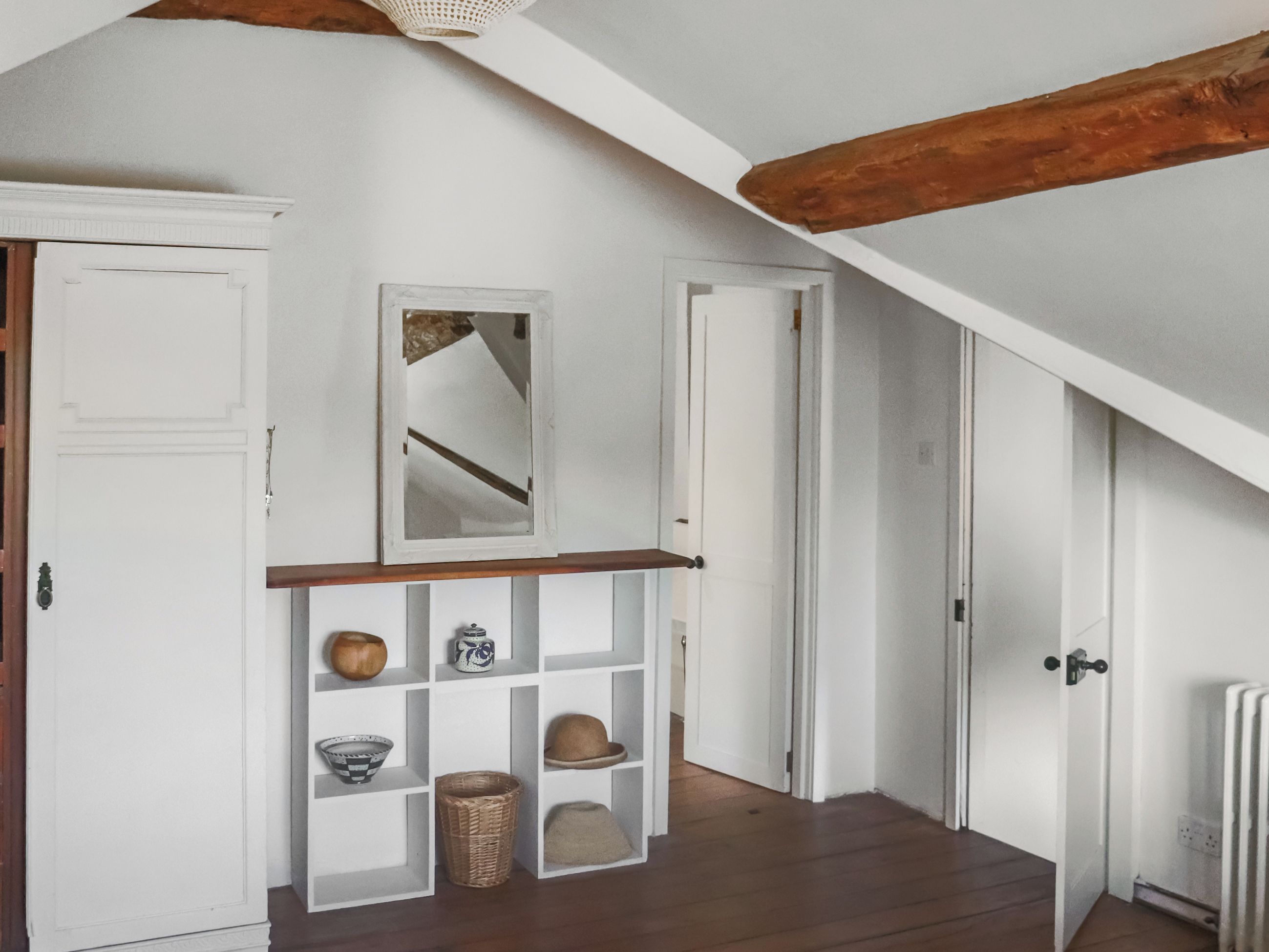 A hallway with white walls, wooden beams, and a shelf with decorative items.
