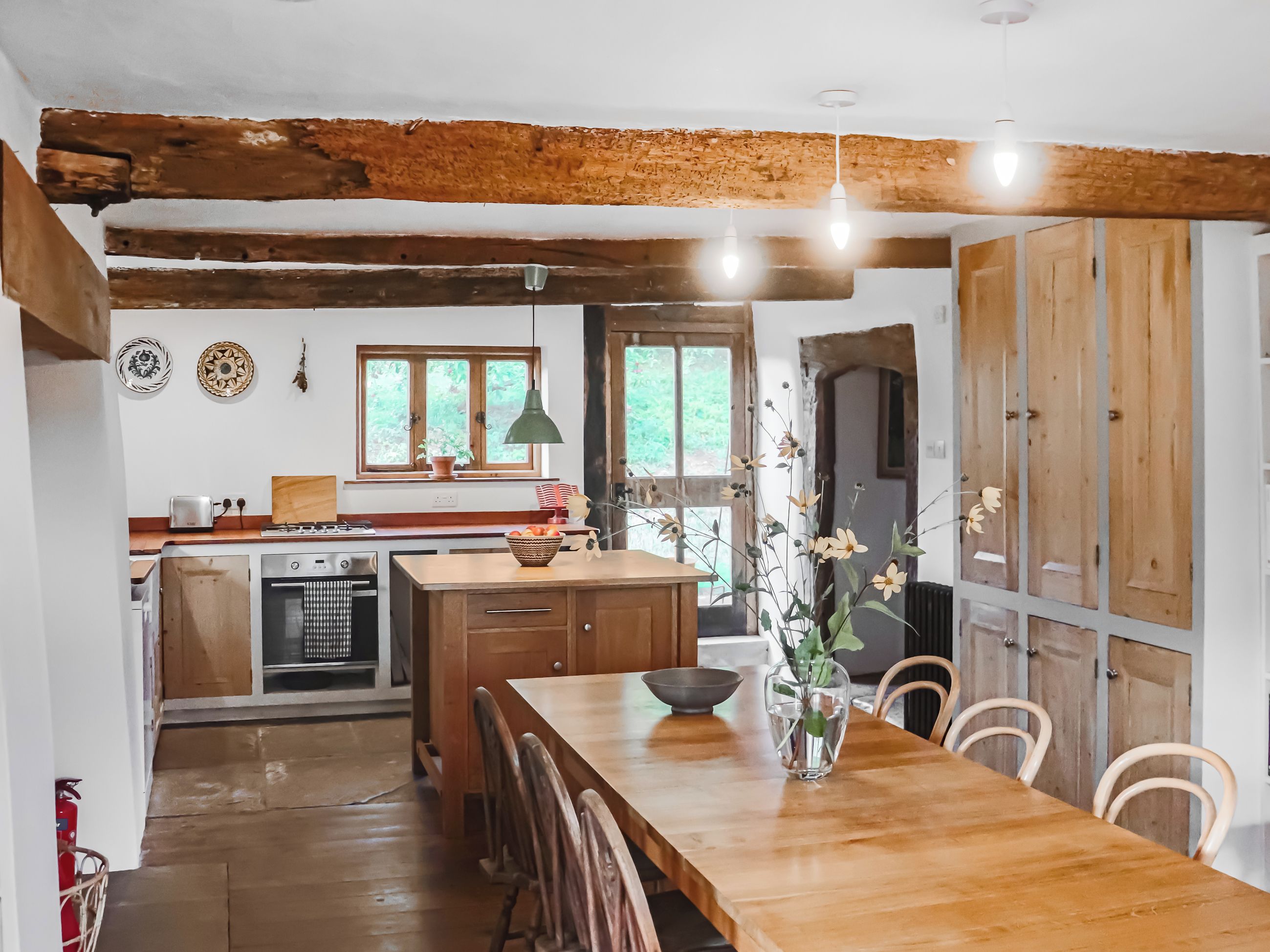 A kitchen with wooden beams, a dining table, chairs, and a vase with flowers.