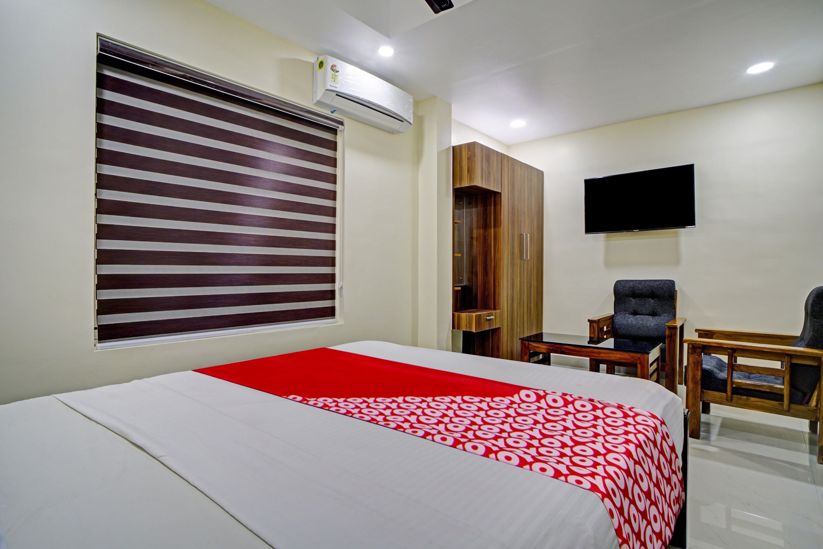 Habitación de hotel con cama, escritorio, silla, armario y televisor de pantalla plana montado en la pared.