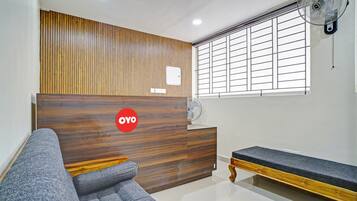 Zona de recepción con un mostrador de madera, un sofá, un banco y una ventana con persianas.