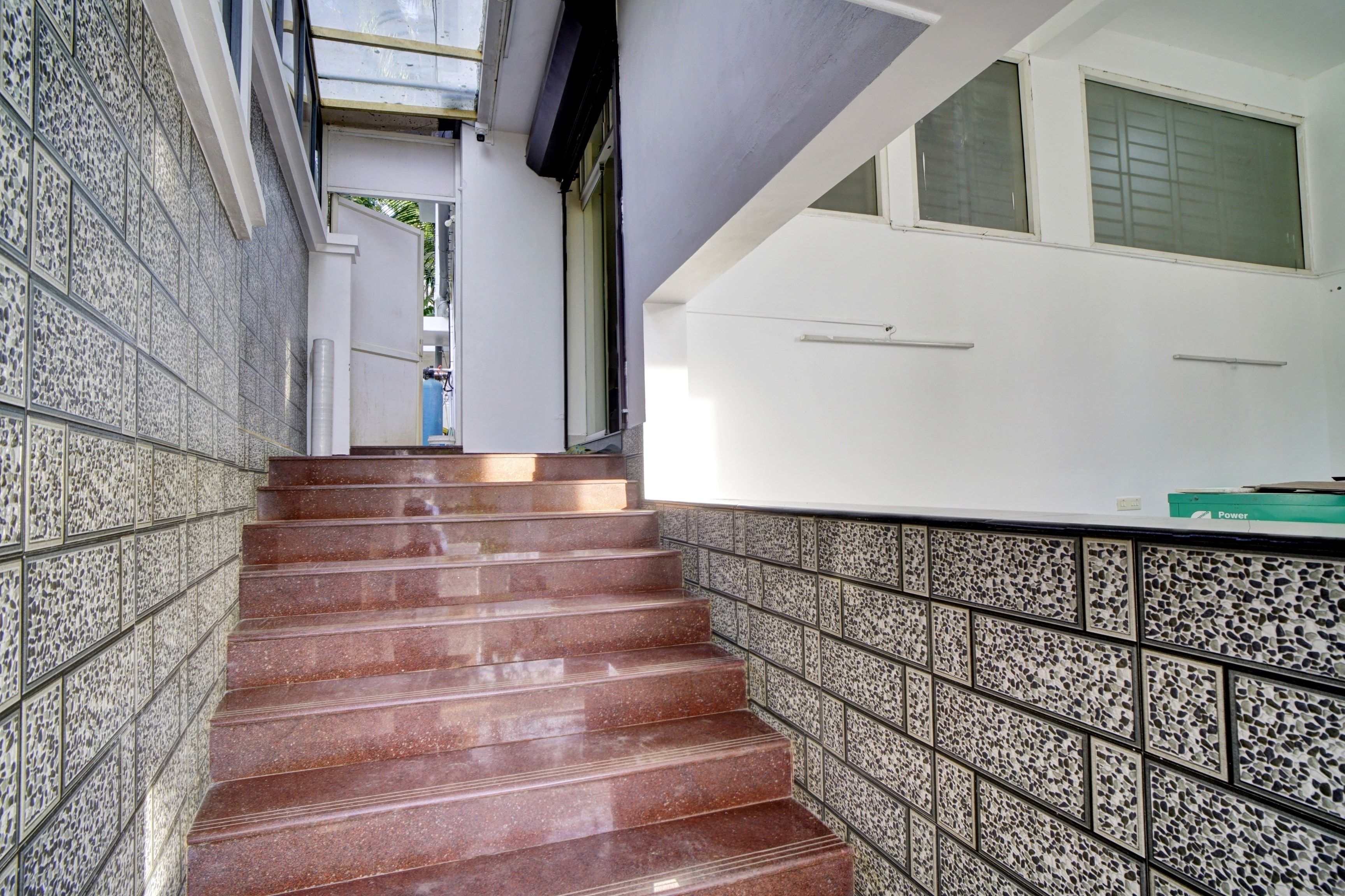 Una escalera con un muro revestido de azulejos a un lado y una pared blanca al otro, que conduce a una habitación con ventana.