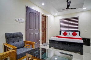 A bedroom with a bed, a chair, a ceiling fan, and a window with blinds. - Hotel O Crystal Executive Suites (Kanayannur)