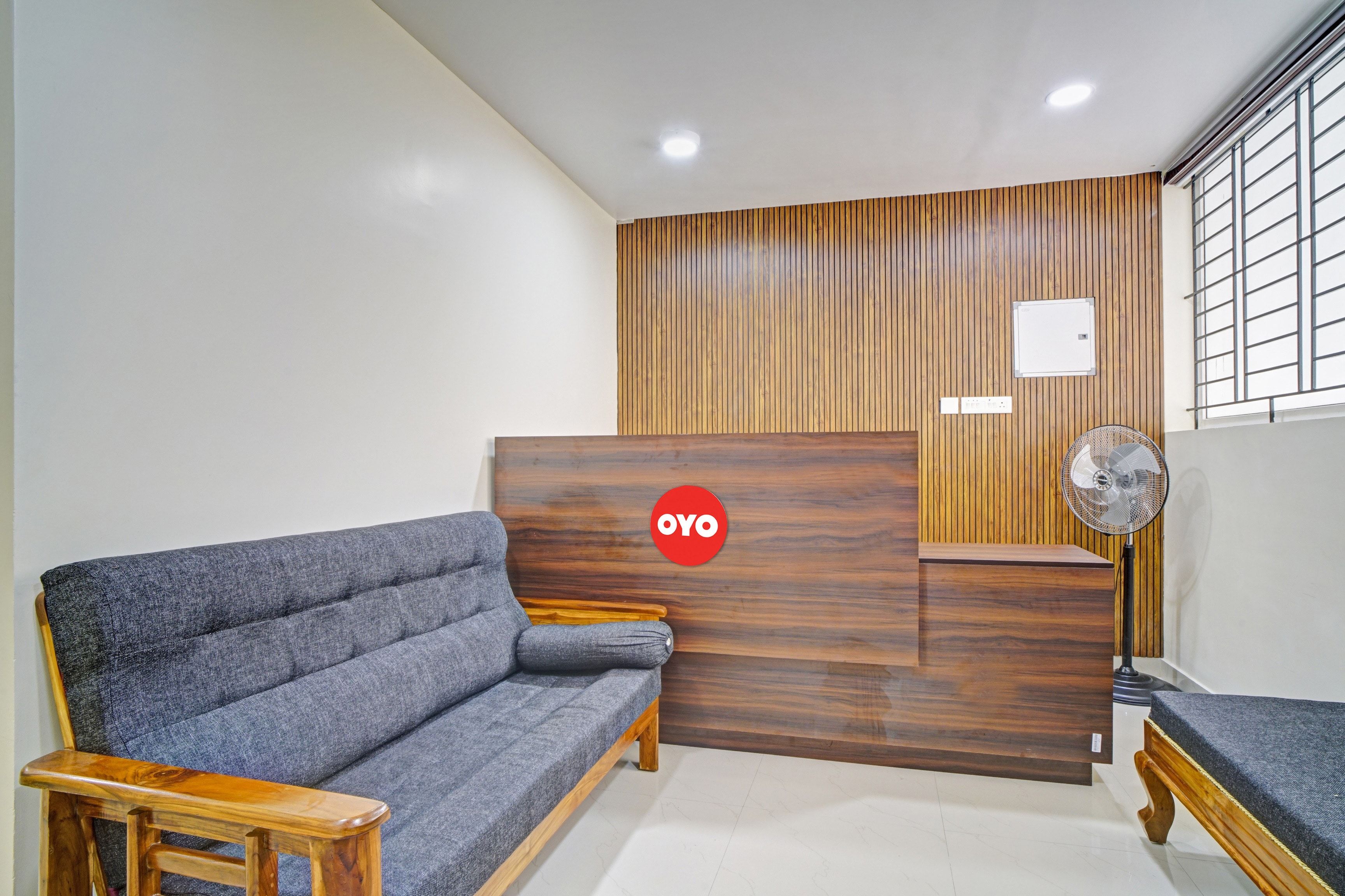 Un área de recepción con un sofá, mostrador de madera y un ventilador.