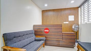 Un área de recepción con un sofá, mostrador de madera y un ventilador.