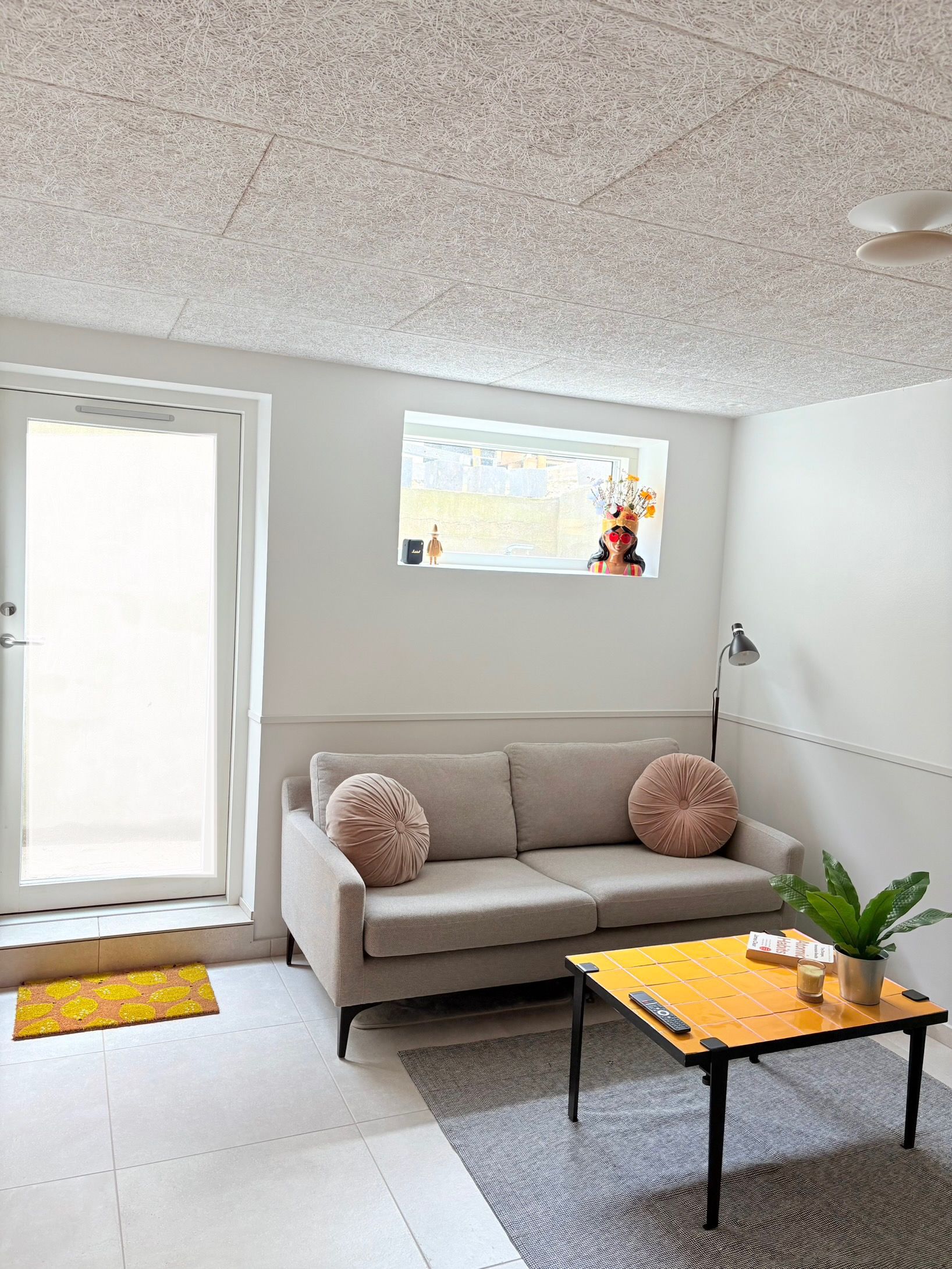 A living room with a sofa, a coffee table, a potted plant, and a window with a view.