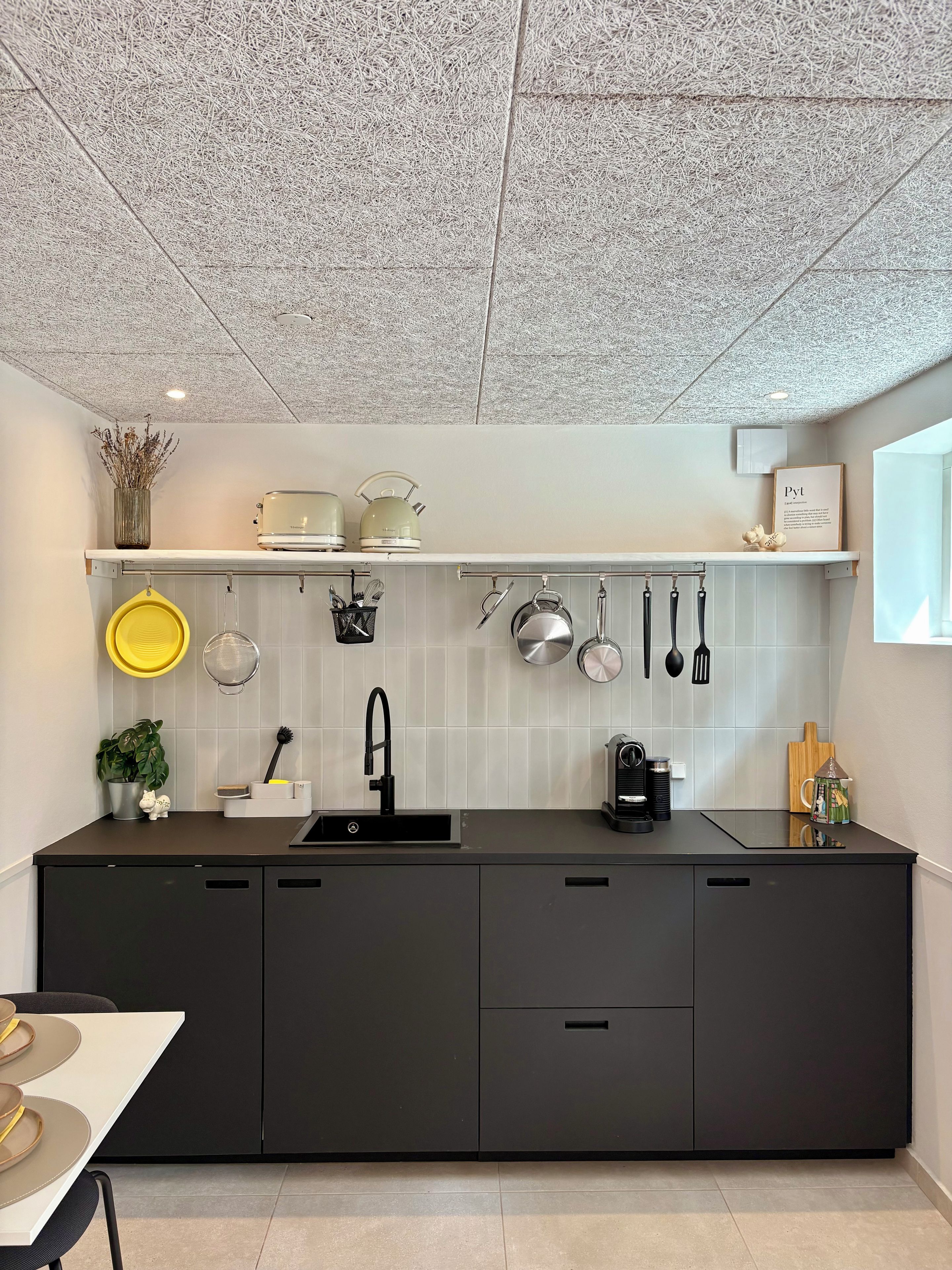Une cuisine moderne avec un plan de travail noir, un revêtement mural blanc et un plafond orné d’un motif texturé.