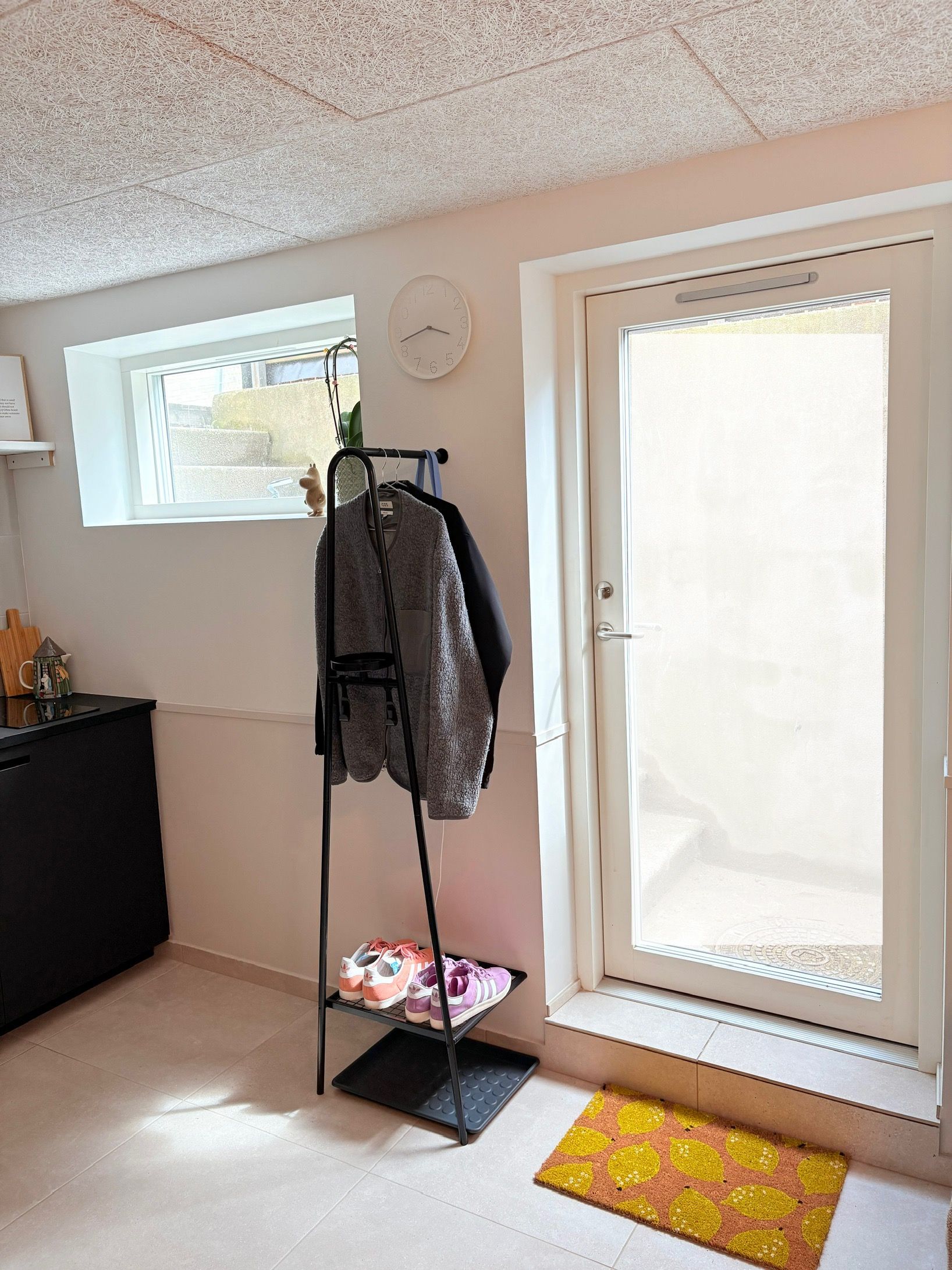 Une pièce avec une porte, une fenêtre, un porte-manteau et un petit tapis.
