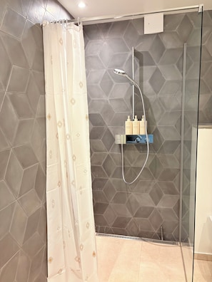 Un espace douche doté d’une porte en verre, d’un pommeau de douche et d’une étagère pour les articles de toilette.