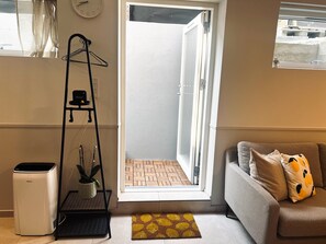 A room with a sofa, a radiator, a small table, a hanging plant, and a window with a view of a brick wall. - New Cozy Basement Studio Apartment! (Rødovre)