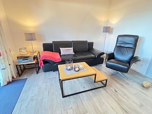 A living room with a black leather sofa, a black leather chair, a wooden coffee table, and a floor lamp. - Rosenhof To Wurth 12a (Busumer Deichhausen)