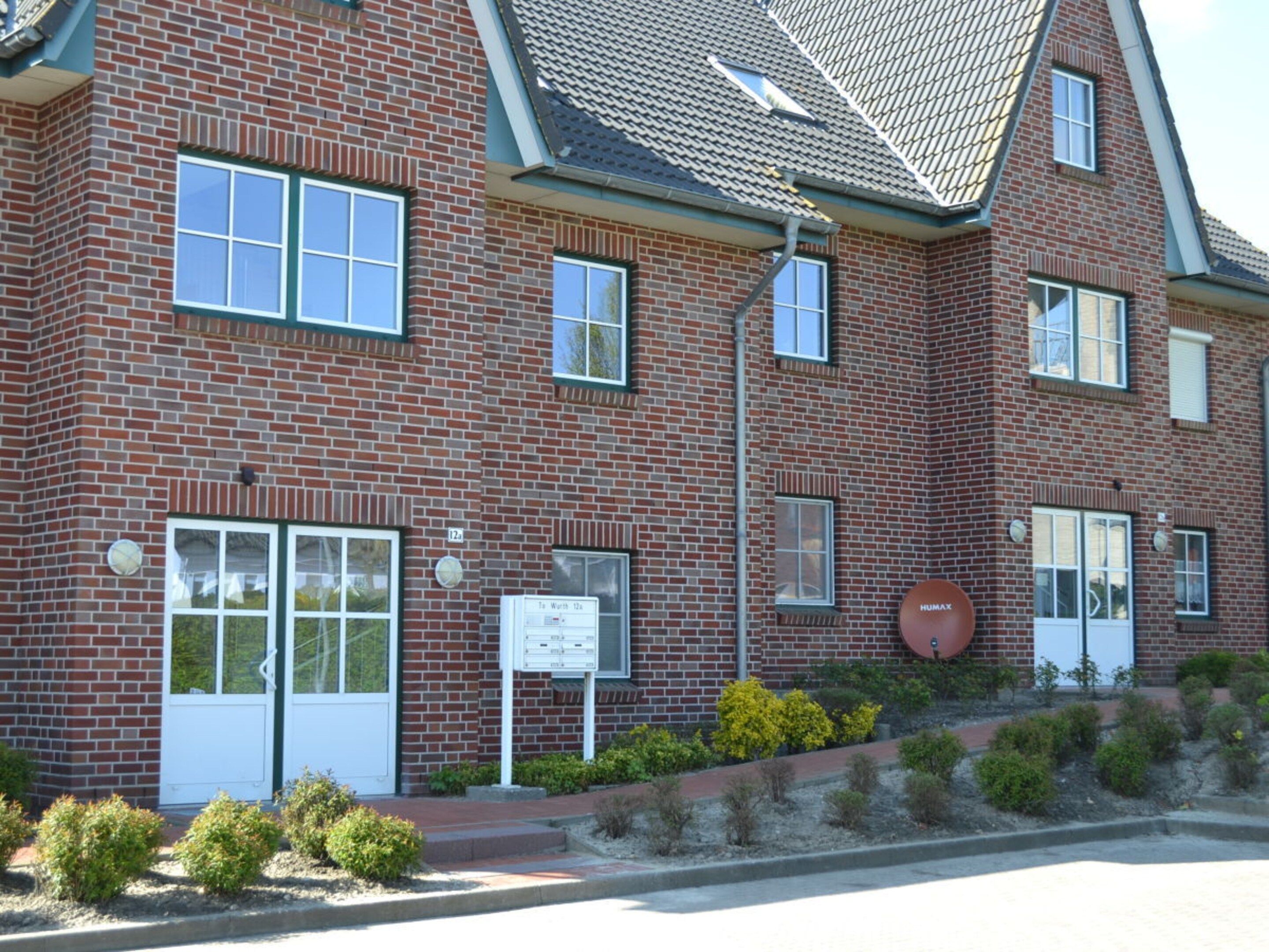 A red brick building with multiple windows, a door, and a small sign.
