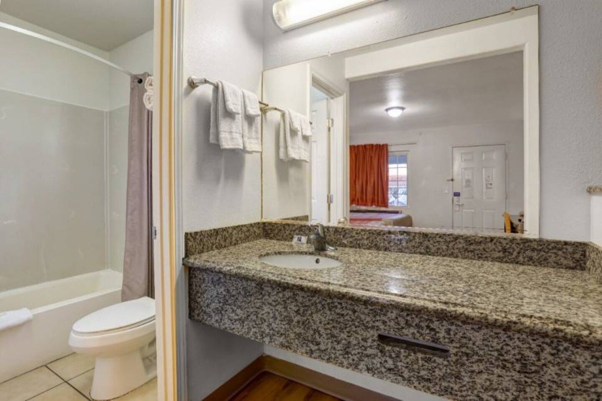 A bathroom with a granite countertop sink, a white toilet, and a shower area.