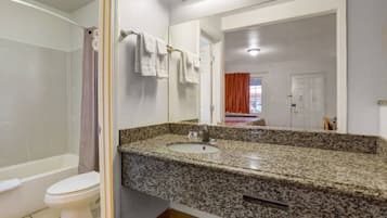 A bathroom with a granite countertop sink, a white toilet, and a shower area.