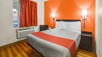 Une chambre d’hôtel équipée d’un lit, d’un climatiseur, d’une fenêtre avec des rideaux et de deux lampes fixées au mur.