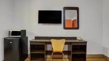 Una habitación con escritorio, silla, televisor y refrigerador.
