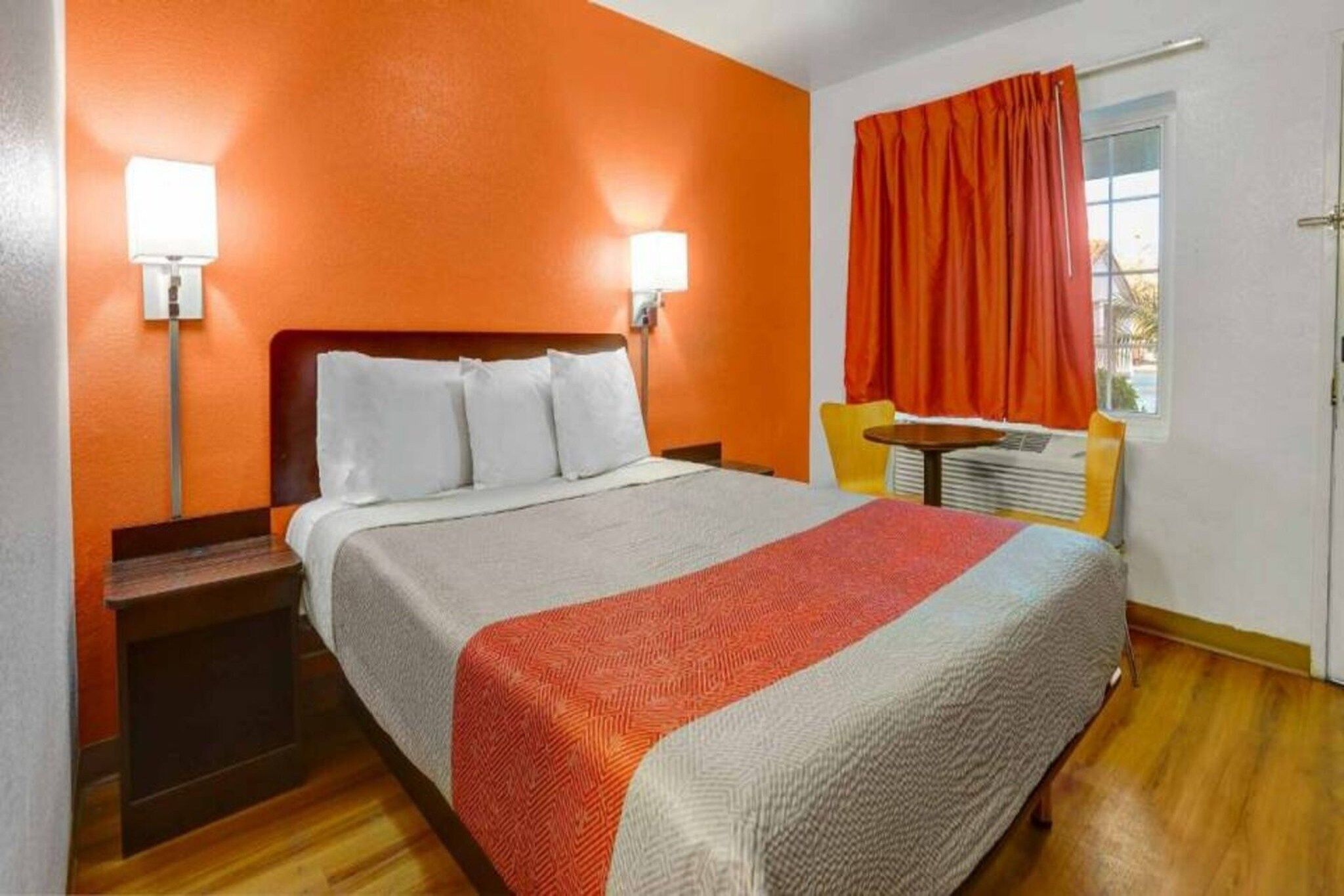 Una habitación de hotel con una cama, mesitas de noche, un ventanal con cortinas y un calefactor en la pared.