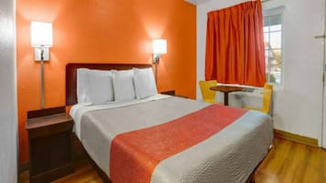 Una habitación de hotel con una cama, mesitas de noche, un ventanal con cortinas y un calefactor en la pared.