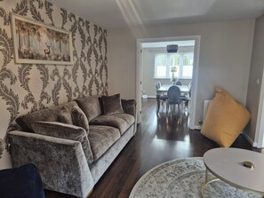A living room with a sofa, a round coffee table, and a dining area with a table and chairs. - The Hideaway - Luxury 4 Bedroom House in Bicester (Oxfordshire)