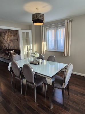 A dining area with a glass table, six chairs, a vase with flowers, and a pendant light. - The Hideaway - Luxury 4 Bedroom House in Bicester (Oxfordshire)