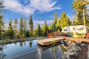 Un espace de loisirs comprenant une piscine, une terrasse en bois et une caravane ancienne garée à proximité.