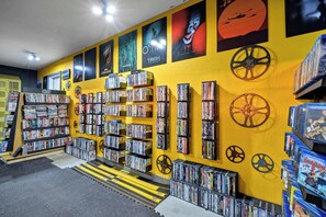 Ein Verleih für Filme mit mehreren Regalen voller DVDs und Blu-rays, einer gelben Wand mit Filmplakaten und einer Treppe, die in die obere Etage führt.