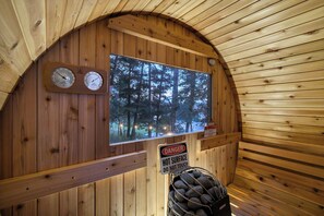 Una sauna con paredes de madera, un termómetro, un higrómetro y un letrero de advertencia sobre superficies calientes.