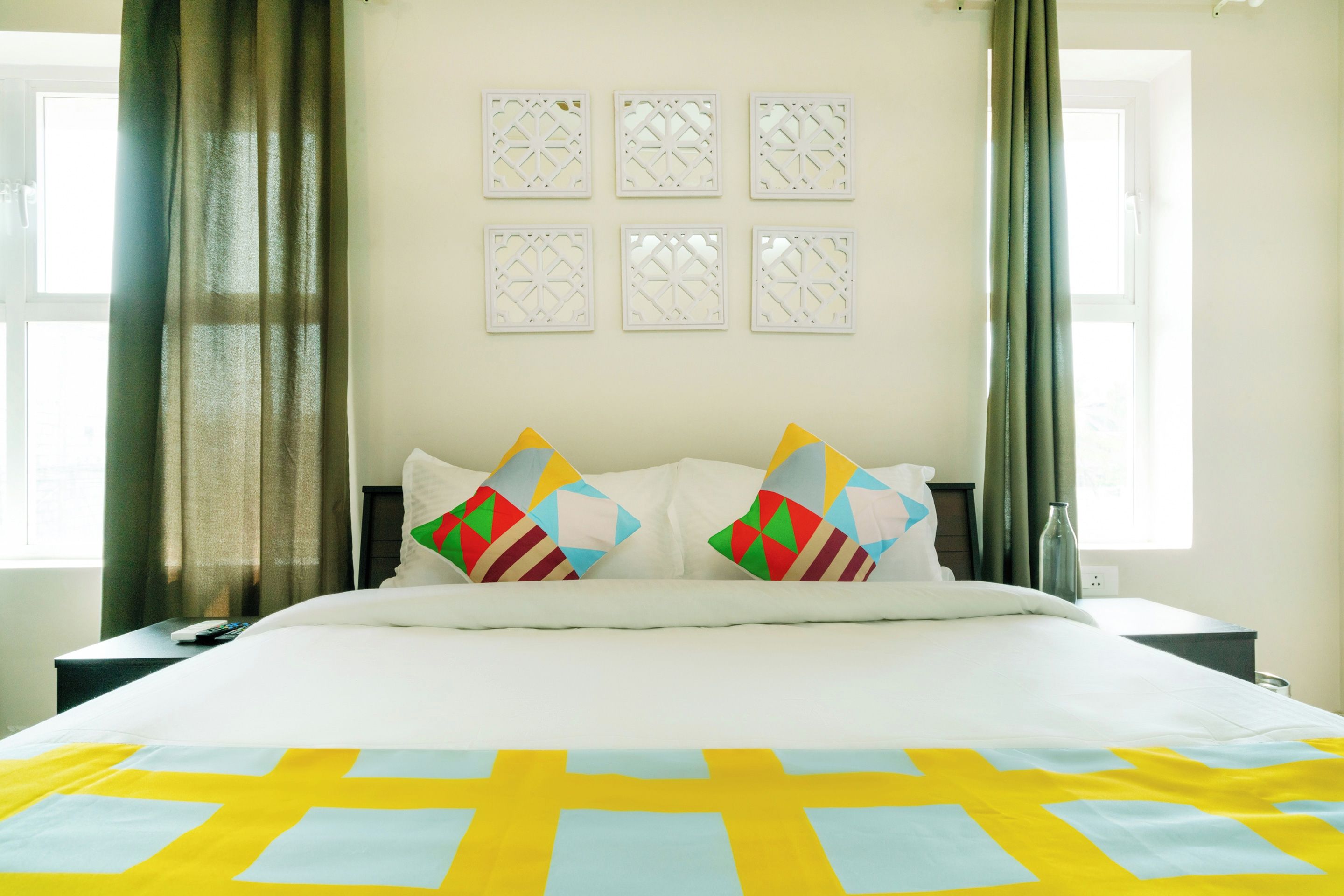 Habitación de hotel con cama, dos mesitas de noche, ventana con cortinas y pared con paneles decorativos.