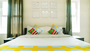Habitación de hotel con cama, dos mesitas de noche, ventana con cortinas y pared con paneles decorativos.