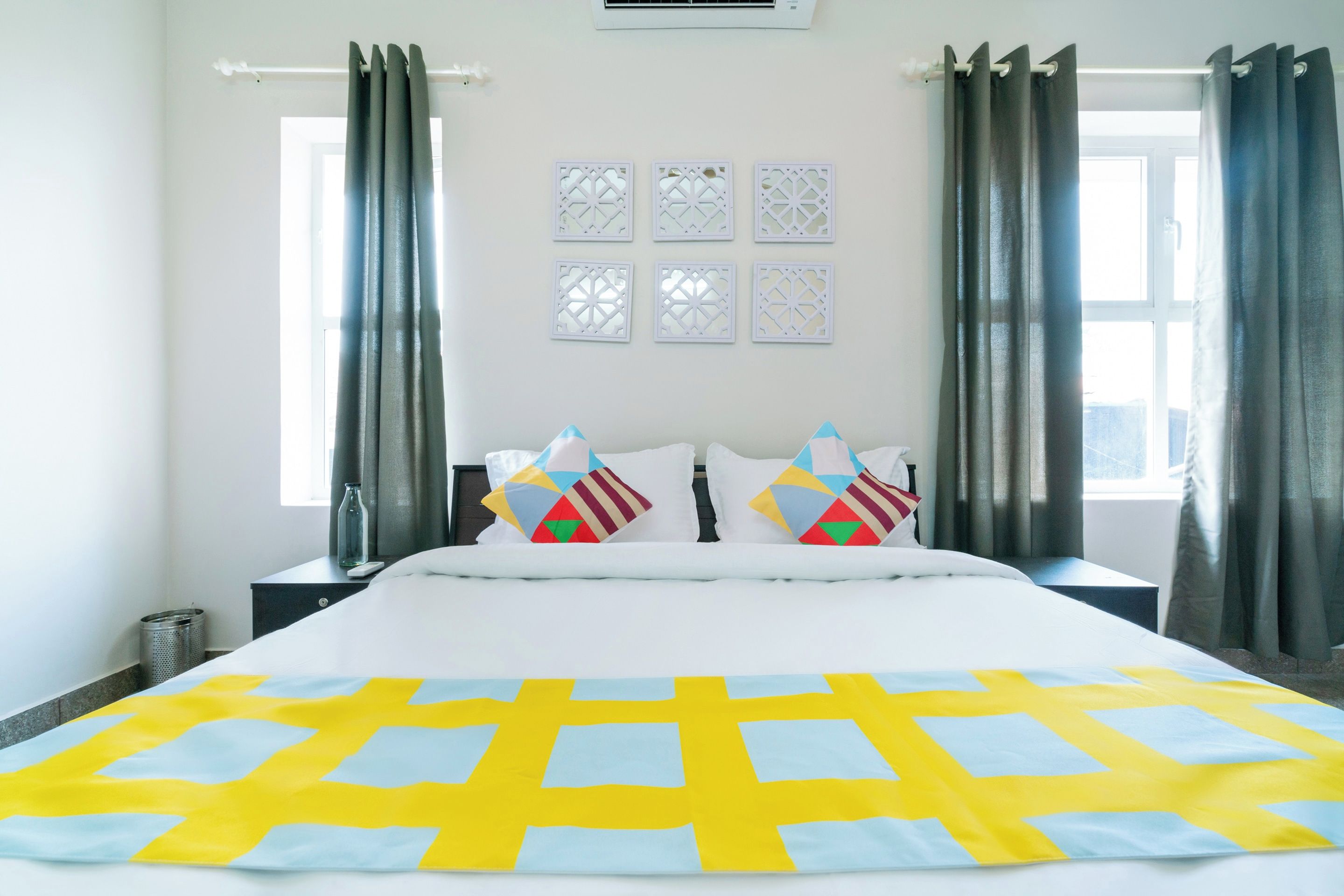 Habitación de hotel con una cama grande, dos mesitas de noche, una ventana con cortinas y paneles decorativos en la pared.