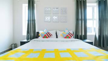 Habitación de hotel con una cama grande, dos mesitas de noche, una ventana con cortinas y paneles decorativos en la pared.