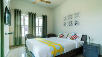 A hotel room with a bed, a desk, a chair, a TV, and a ceiling fan.