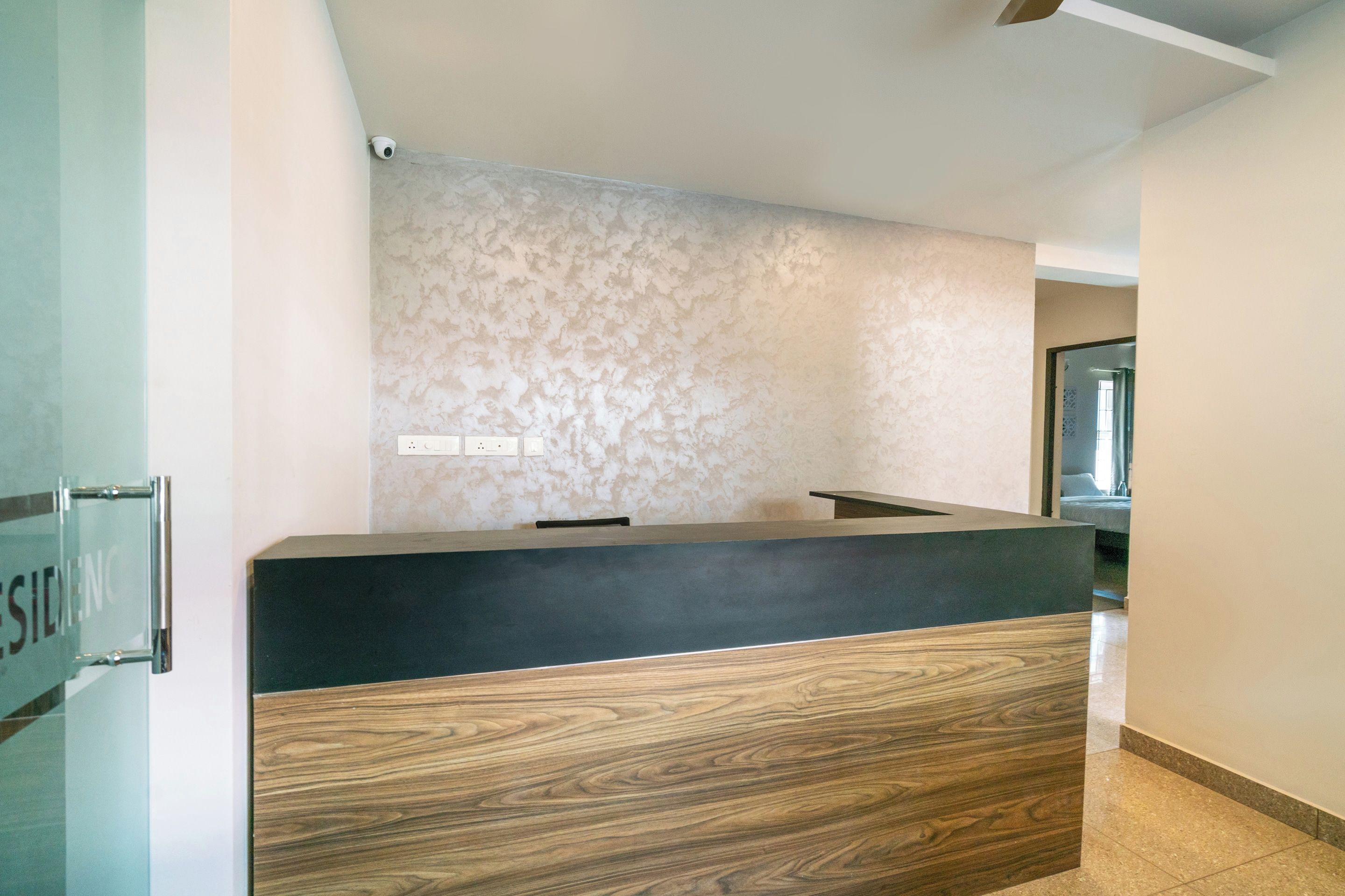 A reception desk with a modern design, a textured wall behind it, and a visible door to the left.