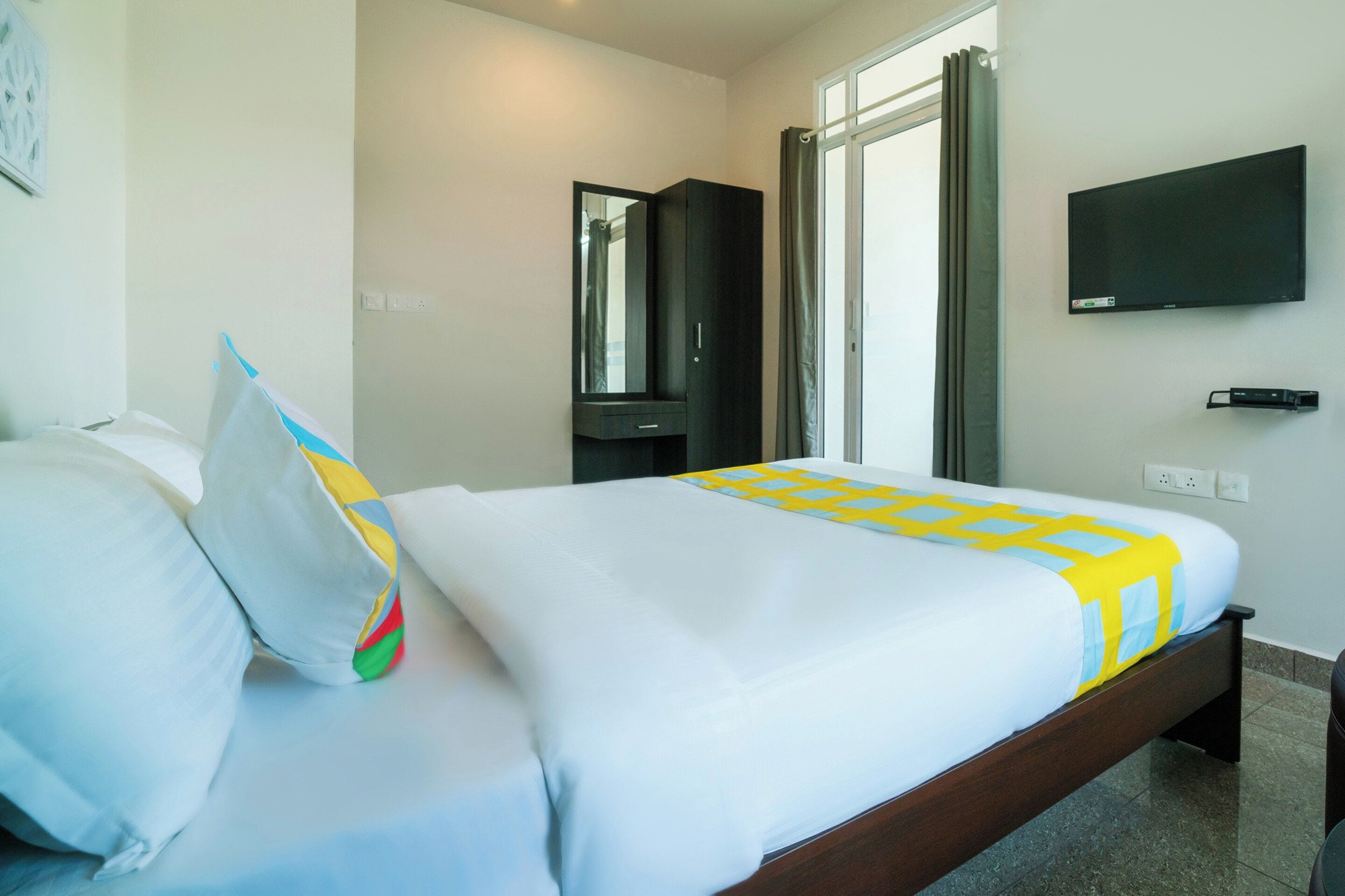 Une chambre d’hôtel avec un lit, un téléviseur fixé au mur et une fenêtre avec des rideaux.