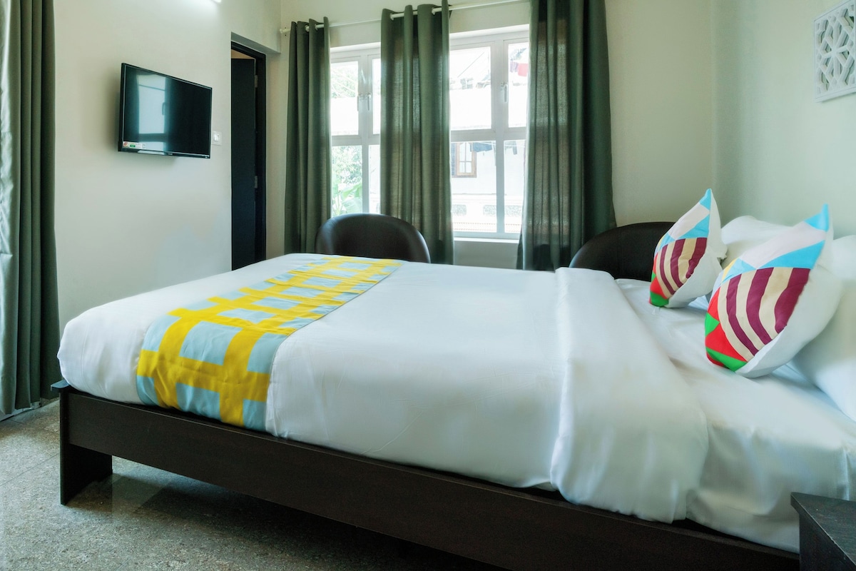 Una habitación de hotel con una cama, un televisor en la pared y un ventanal con cortinas.