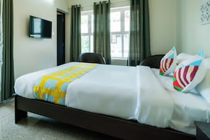 Una habitación de hotel con una cama, un televisor en la pared y un ventanal con cortinas.