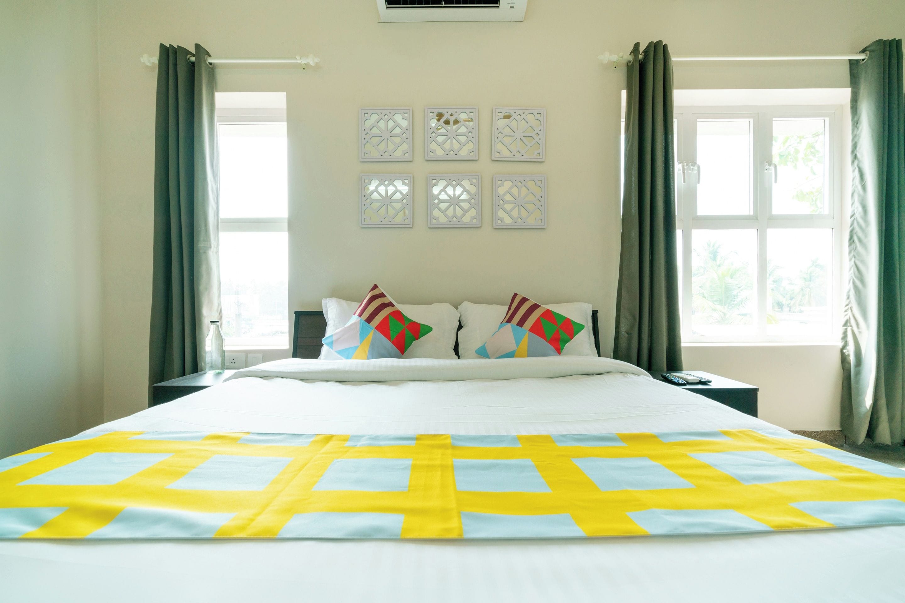 A hotel room with a bed, two bedside tables, a window with curtains, and decorative wall panels.