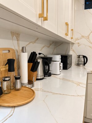 Cozinha moderna com bancadas de mármore branco, eletrodomésticos de aço inoxidável e puxadores dourados nos armários.