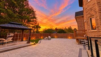 A backyard patio with a covered seating area, a brick patio, and a wooden fence.