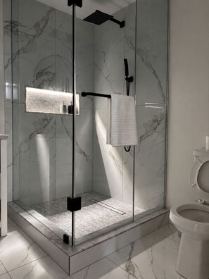 Ein modernes Badezimmer mit einer Glaskabine zur Dusche, einer Toilette und einem Waschbecken mit Marmorrückwand.