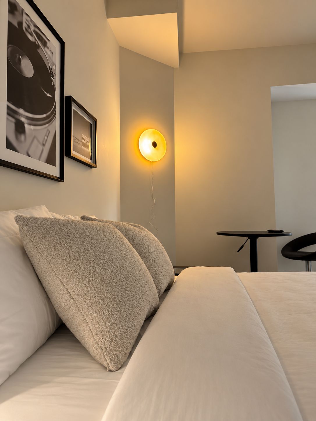 Ett hotellrum med en säng, två kuddar, en väggmonterad lampa och en inramad tavla.