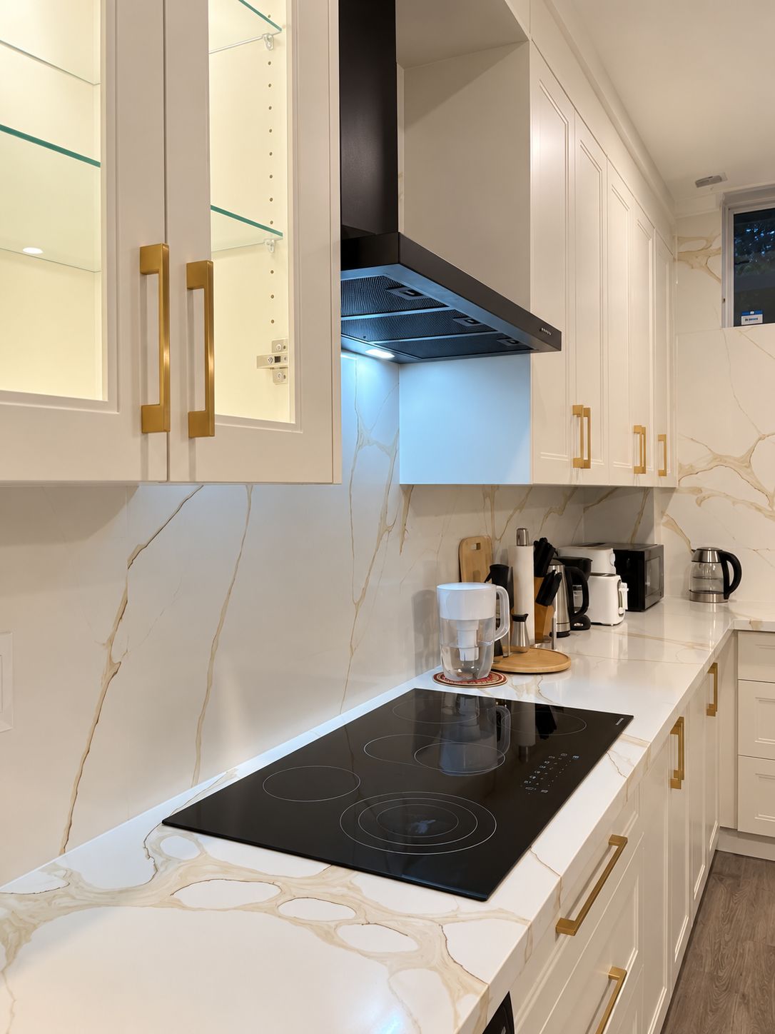 Une cuisine moderne avec des meubles blancs, une plaque de cuisson à induction noire et une machine à café.