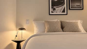 A bedroom with a bed, pillows, a nightstand with a lamp, and two framed pictures on the wall.