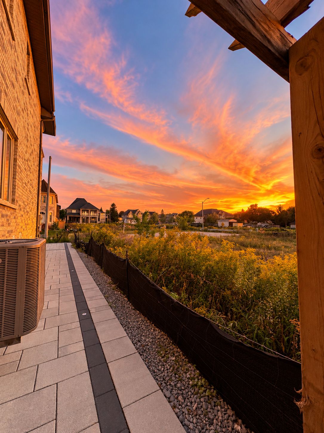 A residential area with a paved walkway, a wooden fence, and houses in the background.