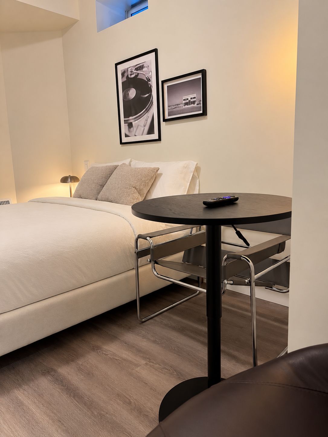 A modern hotel room with a bed, a small round table, and a sofa. There are two framed pictures on the wall.