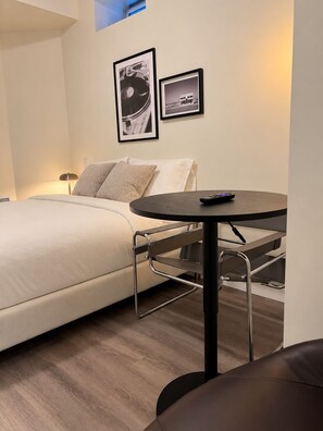 Quarto de hotel moderno com uma cama, uma mesinha redonda e um sofá. Há duas quadros na parede.