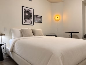 Ein modernes Schlafzimmer mit einem großen Bett, zwei gerahmten Bildern an der Wand, einem Nachttisch und einer Wandlampe.